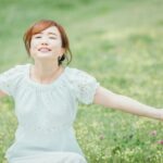 草地で腕を広げて深呼吸する女性