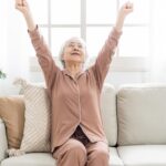 ソファで両腕を広げ伸びをする高齢女性