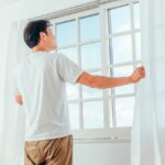 窓辺でカーテンを開け伸びをする男性