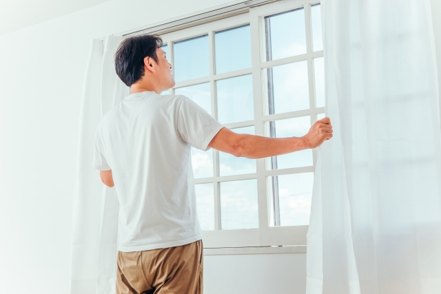 窓辺でカーテンを開け伸びをする男性